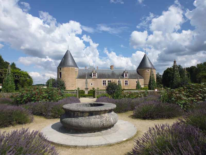 Château de Chamerolles aux tours rondes entouré de jardins fleuris et de parterres de lavande sous un ciel bleu, offrant une 
							atmosphère paisible et un cadre historique en Île-de-France