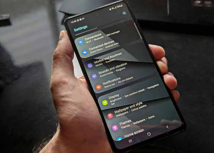 Main tenant un smartphone affichant le menu des paramètres Android, avec les options de connexion et d’affichage