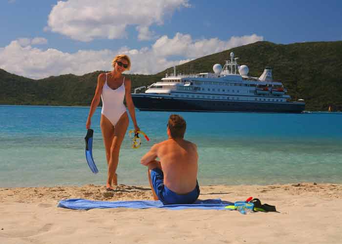 Photo d'une jeune femme en maillot de bain une pice qui sort de la mer avec des palmes  la main, avec un bateau de 
											croisire pour clibataires en arrire plan