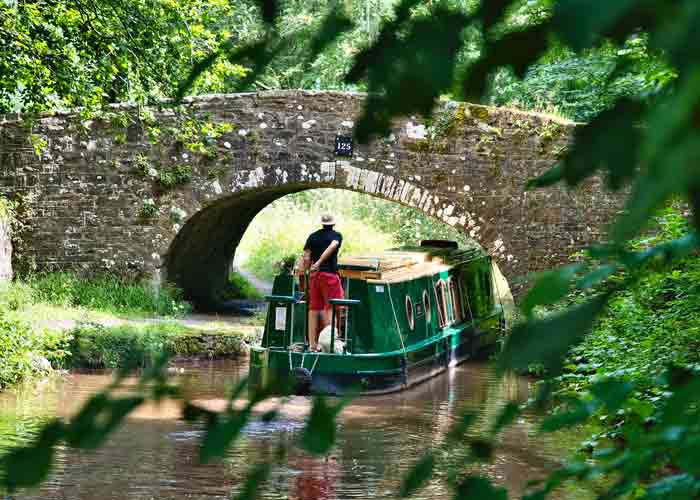 photo d'une petite pniche verte qui passe sous un pont en pierre