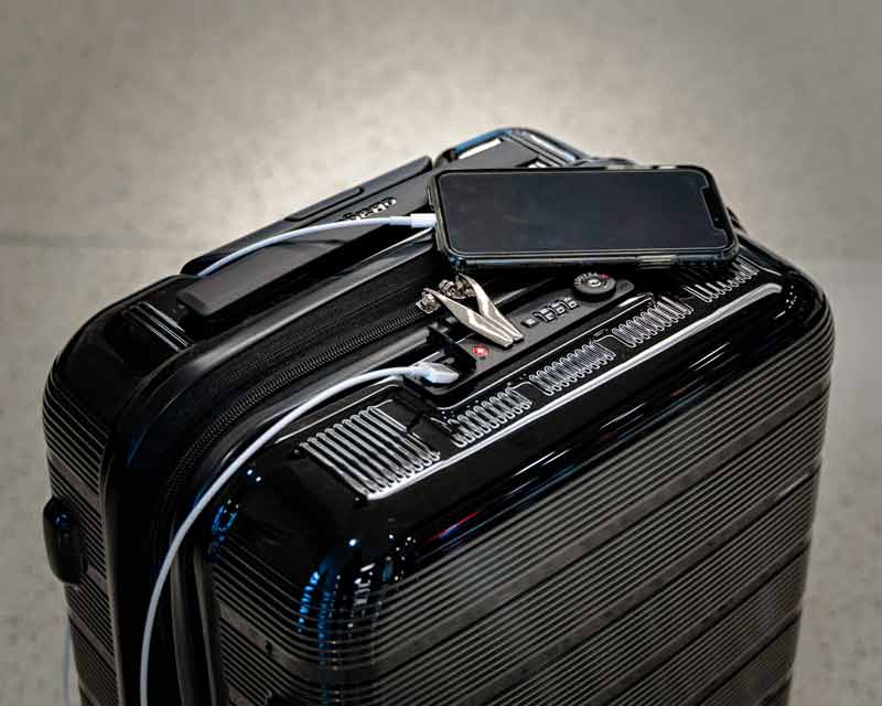 Valise noire rigide avec un téléphone portable, un câble de recharge et un coupe-ongles posés dessus, illustrant les essentiels à emporter pour un long voyage