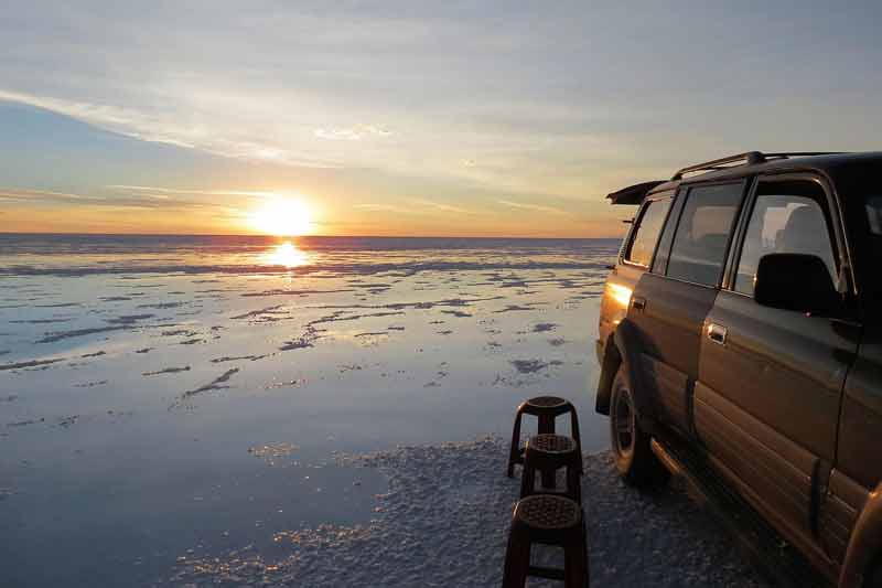 Coucher de soleil sur le Salar d'Uyuni en Bolivie, avec un 4x4 garé sur la surface miroitante du désert de sel