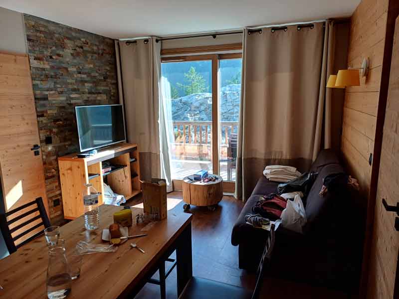 Salon tout en bois d'un appartement en résidence de tourisme à la montagne, avec vue sur les sommets depuis le balcon