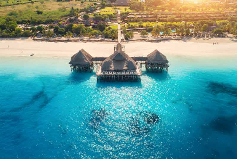 Ponton avec toits en chaume s'avançant sur une mer turquoise à Zanzibar, entouré de plages de sable blanc et de végétation luxuriante