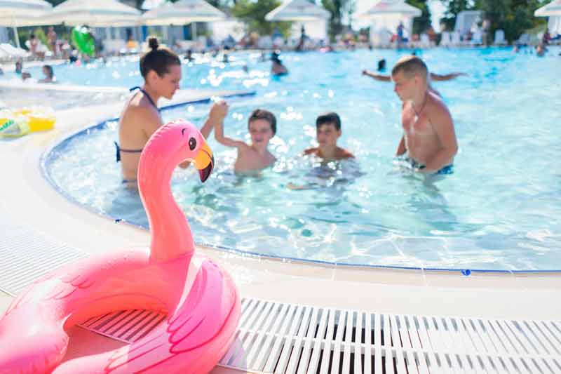 Famille avec enfants s’amusant dans une piscine de camping avec une bouée flamant rose au premier plan