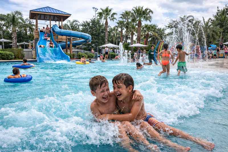 Enfants riant dans une piscine à vagues d’un camping avec des toboggans en arrière-plan