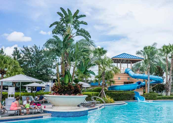 Parc aquatique de camping avec grande piscine, toboggan et palmiers dans une ambiance vacances