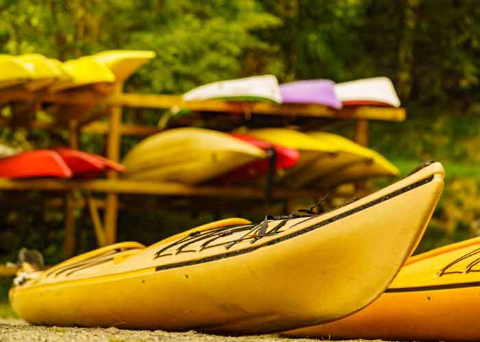 Kayaks jaunes align�s au premier plan, avec plusieurs embarcations color�es rang�es sur des supports en bois dans un cadre naturel verdoyant