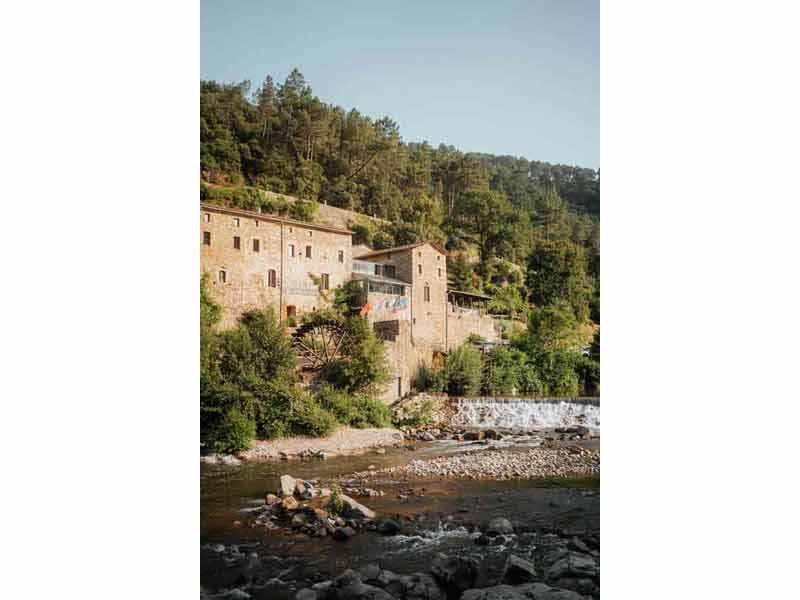 Village d’Anduze dans les Cévennes, maisons en pierre au bord du Gardon avec ancien moulin et roue à eau, entouré de collines boisées