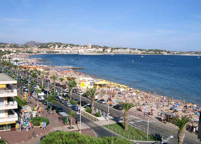 Vue panoramique de la plage de Fréjus, bordée de palmiers avec la mer Méditerranée et des collines en arrière-plan