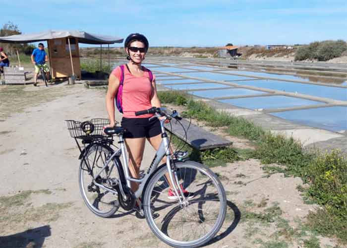 Cycliste souriante posant devant les marais salants de Loix sur l’île de Ré, symbole d’un tourisme nature et à vélo