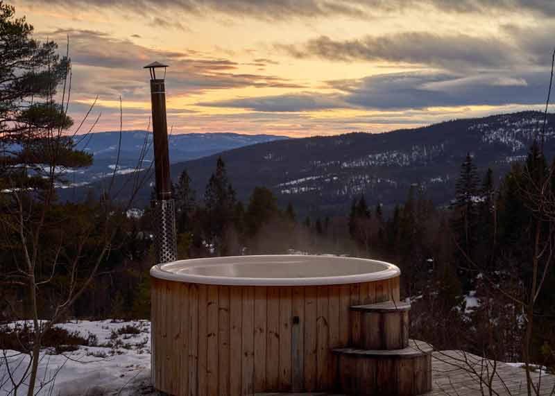 Bain nordique en bois face aux montagnes vosgiennes au coucher du soleil