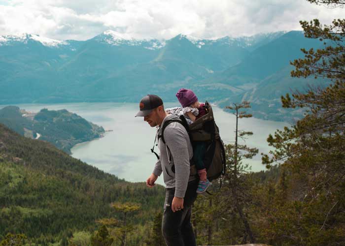P�re en randonn�e avec b�b� en porte-b�b� dorsal face � un lac et paysage de montagne panoramique