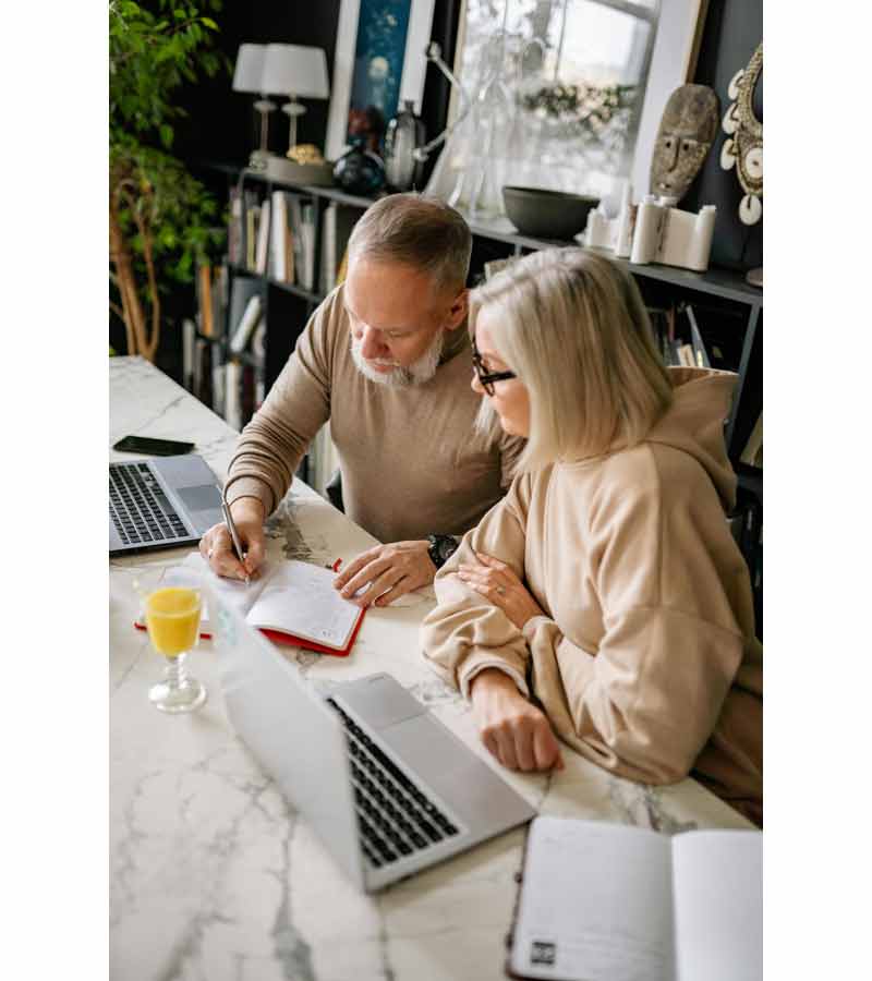 Couple organisant un voyage à domicile avec ordinateur portable et carnet de notes, planification de séjour en ligne