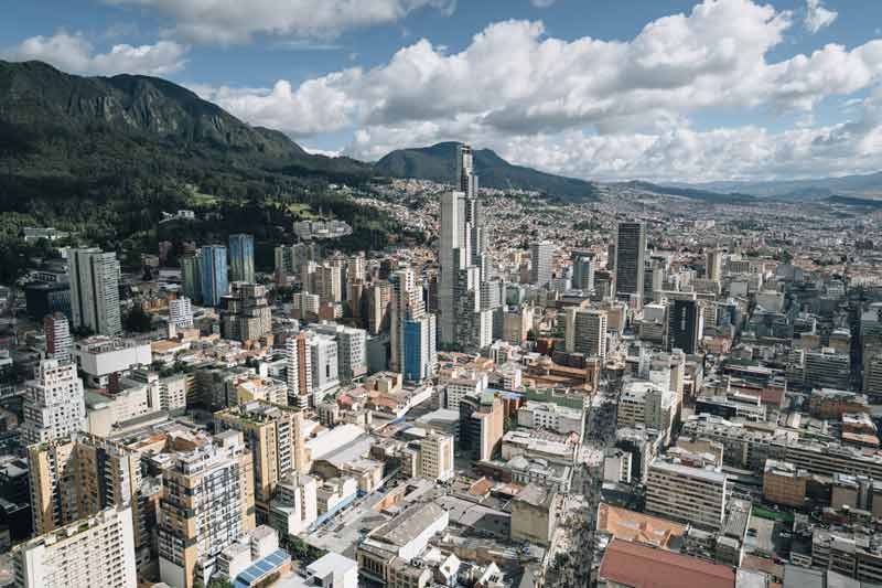 Vue aérienne de Bogotá, Colombie, avec des gratte-ciels modernes, des bâtiments urbains et des collines verdoyantes en arrière-plan sous un ciel partiellement nuageux