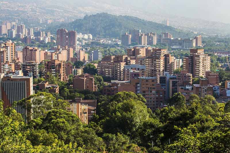 Vue de Medellín, Colombie, avec des immeubles en briques rouges entourés de collines verdoyantes et d'une végétation dense, sous un ciel légèrement brumeux