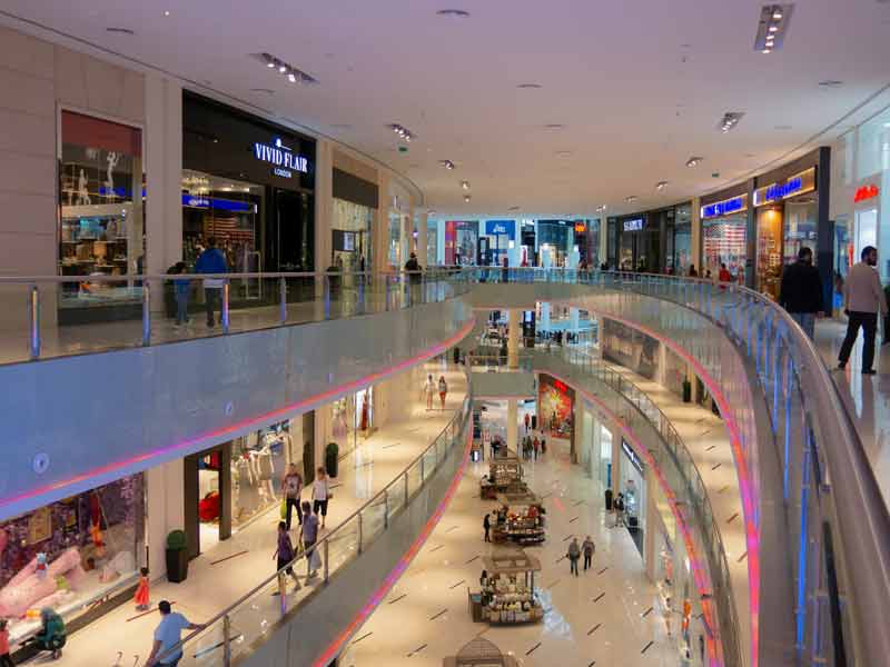 Intérieur d'un centre commercial moderne à Dubaï, avec plusieurs étages, des boutiques de luxe, des passerelles en verre et 
							des visiteurs flânant dans les allées éclairées