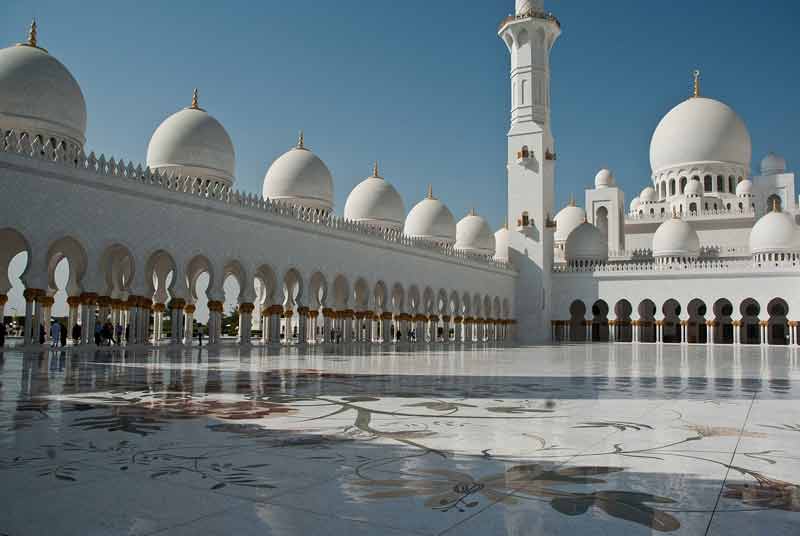 Vue de la cour intérieure de la grande mosquée Sheikh Zayed à Abou Dabi, avec ses dômes blancs immaculés, ses arches élégantes 
							et son sol en marbre orné de motifs floraux