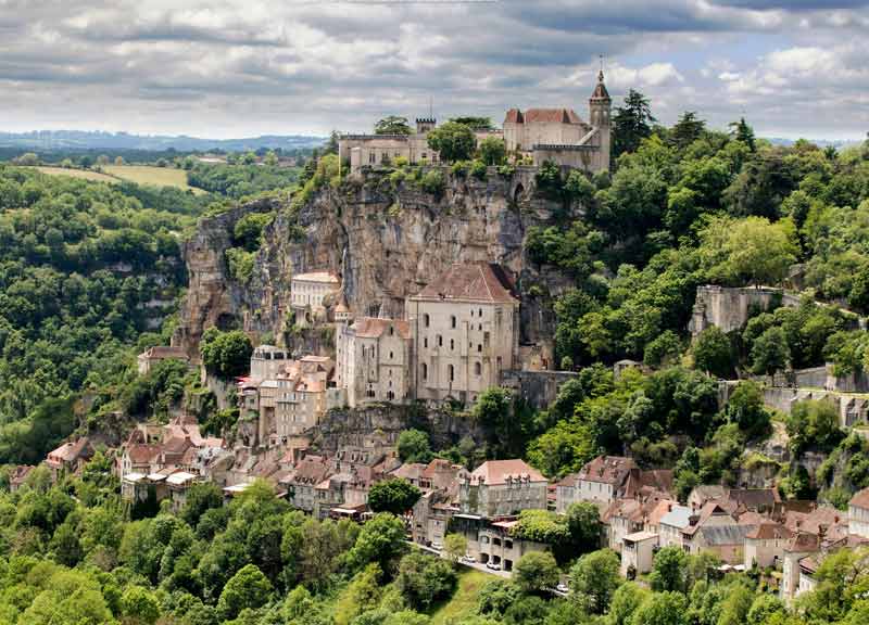 Vue panoramique du village de Rocamadour, accroché à une falaise, avec ses bâtiments médiévaux, son sanctuaire et une verdoyante vallée en arrière-plan