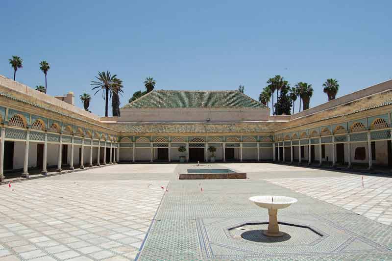 Cour intérieure du Palais de la Bahia à Marrakech, avec ses arcades élégantes, son sol en mosaïque et sa fontaine centrale sous un ciel bleu