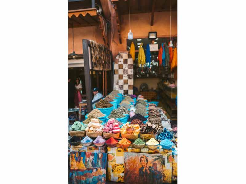 Étal coloré d’un souk à Marrakech, présentant des épices, des pigments et des produits artisanaux sous une lumière chaleureuse