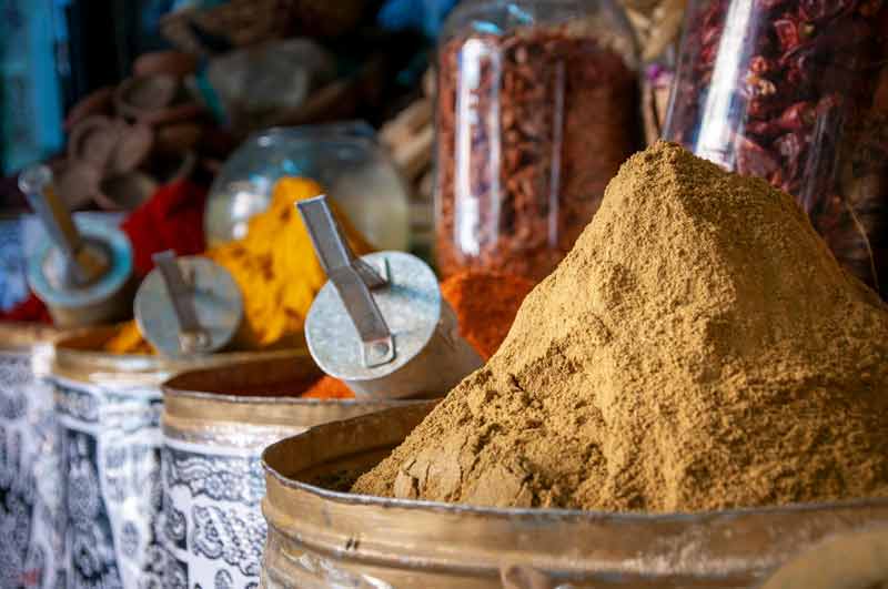 Monticules d’épices colorées dans un souk de Marrakech, avec des pots en verre remplis de piments et d’autres condiments en arrière-plan