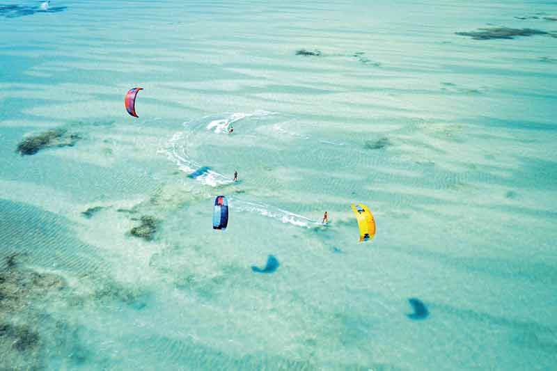 Vue aérienne de kitesurfeurs glissant sur les eaux peu profondes et cristallines de Zanzibar, avec des voiles colorées contrastant avec le lagon turquoise